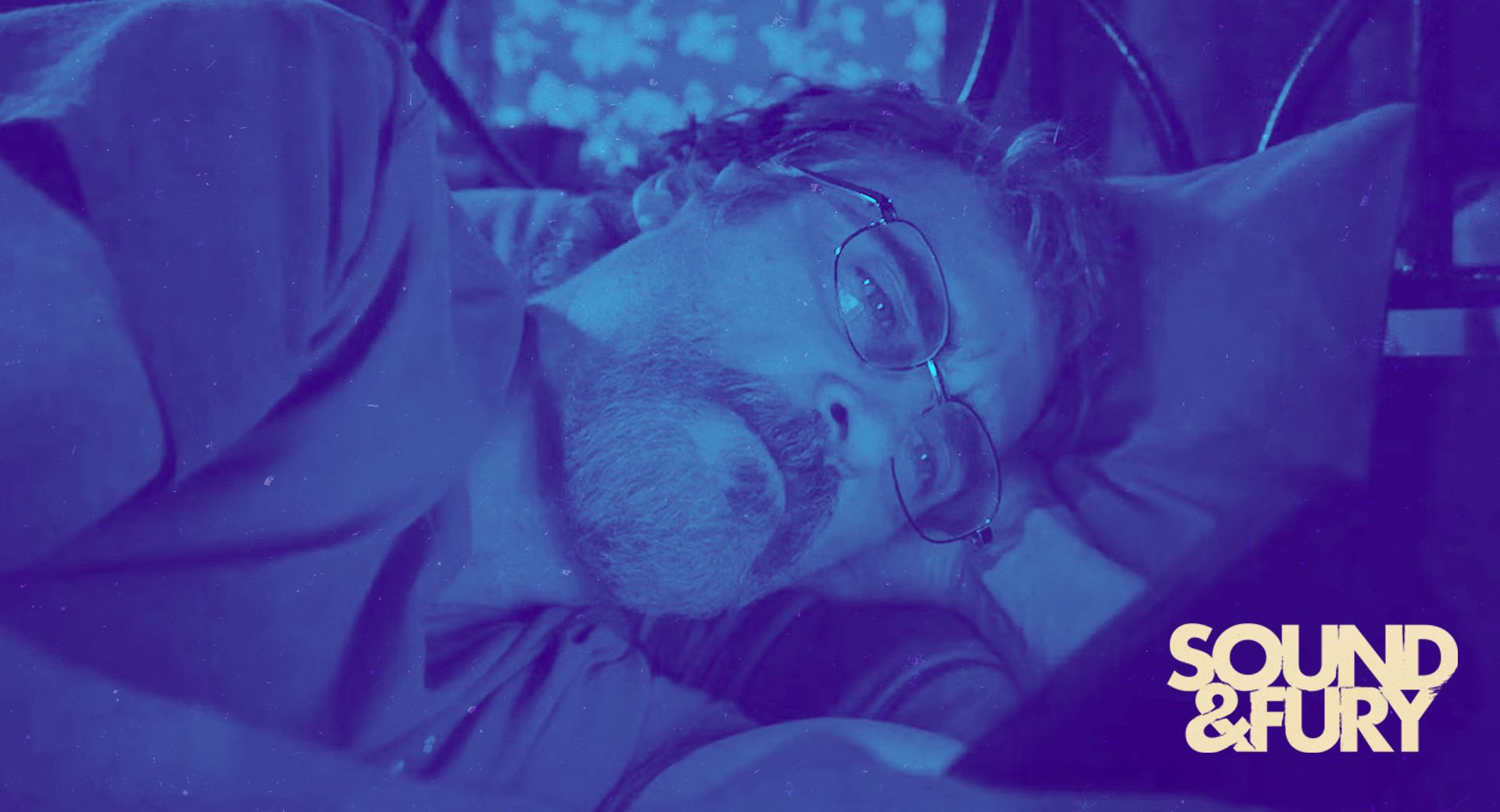 Cyan-toned close-up of Gavin in bed, glasses askew, lost in thought