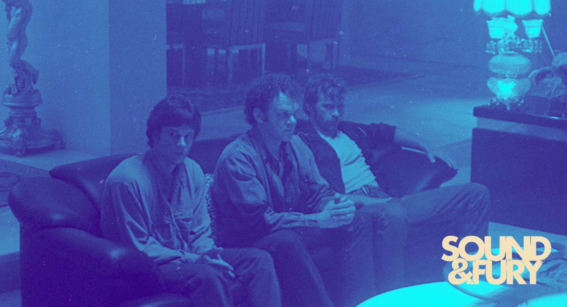 Three men on a couch in a tense quiet moment — tonal reference